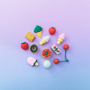 miniature sweets: ice cream, cake, cupcake, donut, pastries laid out on a gradient   pink and blue background. the concept of food and dessert. fashion minimal. pastel colors. flat lay, top vew