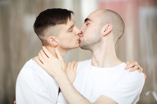 Young homosexual couple kissing tenderly while standing in embrace