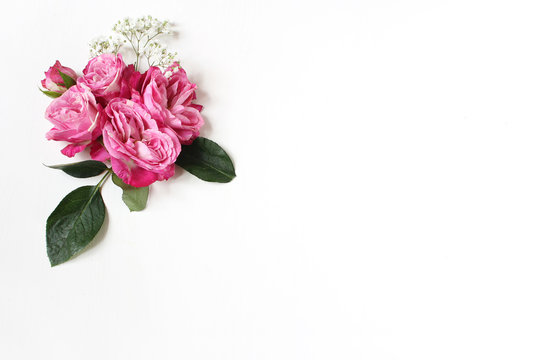 Decorative floral composition with pink roses, green leaves and and baby's breath Gypsophila flowers on white table background. Flat lay, top view. Wedding or birthday styled stock photo.