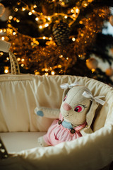 A toy in a cradle near christmas tree with the lights on. Parenting or christmas celebrations concept
