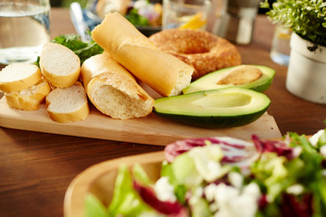Fresh wheat bread and avocado halves on wooden board on table