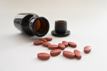 Brown tablets and opaque bottles on white background. Some medicines should be stored in opaque containers to prevent deterioration.