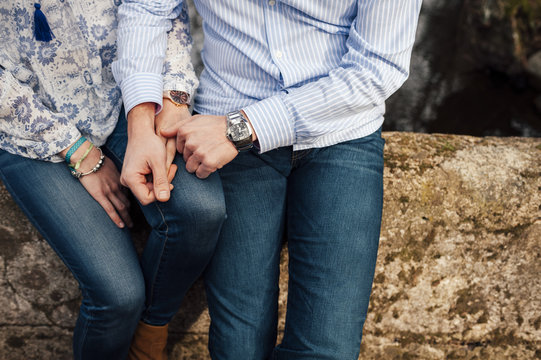 Midsection of young stylish couple holding hands seated on a rocky wall