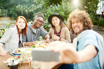 Group of young friends making selfie by served table during festive dinner