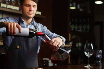 Sommelier pouring wine into glass from decanter. Male waiter