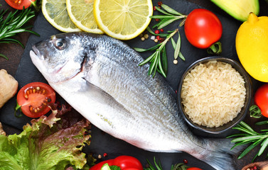 Food background. Fresh, raw Dorado with a swallow, lemon, avocado on a dark concrete background.