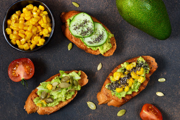 Toasts with avocado, corn tomato and cucumber on a brown background.