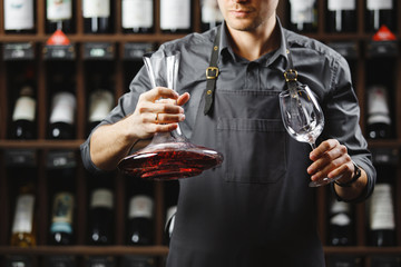 Barman in apron holds vessel with red wine and glass