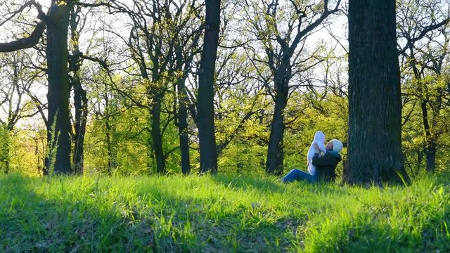 Mother plays with her baby in a spring park under a big oak tree.