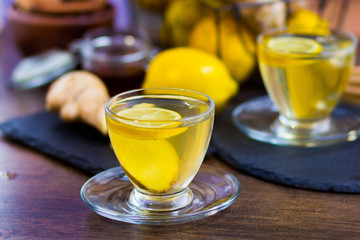 Glass cup of hot tea with mint, honey, ginger and lemon on dark background.