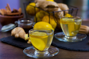 Glass cup of hot tea with mint, honey, ginger and lemon on dark background.