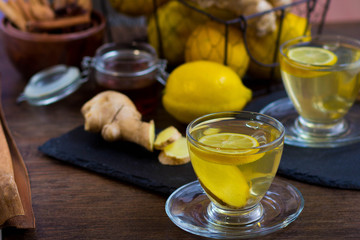 Glass cup of hot tea with mint, honey, ginger and lemon on dark background.