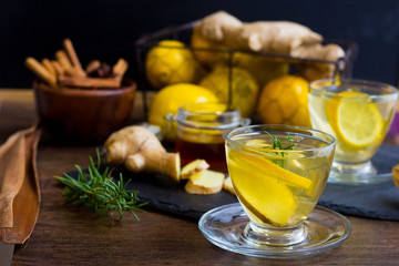 Glass cup of hot tea with mint, honey, ginger and lemon on dark background.