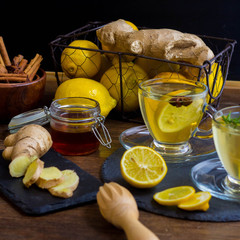 Glass cup of hot tea with mint, honey, ginger and lemon on dark background.