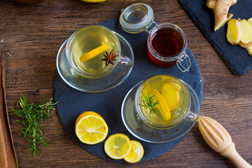 Glass cup of hot tea with mint, honey, ginger and lemon on dark background.