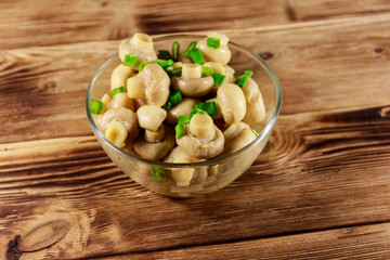 Glass bowl with pickled champignons. Marinated mushrooms on wooden table