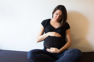 Young expecting female sitting at home on a couch and touching her belly