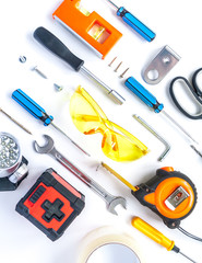 Top view of working tools, wrench, screwdriver, level, tape measure, bolts, and safety glasses on a white background.