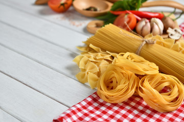 Pasta spaghetti, farfalle, linguine with vegetables and spices on white wooden table