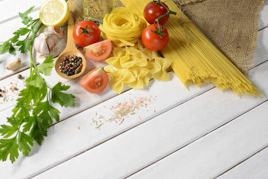 Pasta spaghetti, farfalle, linguine with vegetables and spices on white wooden table