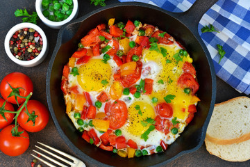 Eggs with tomatoes, pepper and green peas in a frying pan on a concrete background.