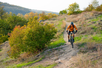 Obraz premium Cyclist in Orange Riding the Mountain Bike on the Autumn Rocky Trail. Extreme Sport and Enduro Biking Concept.