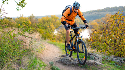 Naklejka na ściany i meble Cyclist in Orange Riding the Mountain Bike on the Autumn Rocky Trail. Extreme Sport and Enduro Biking Concept.
