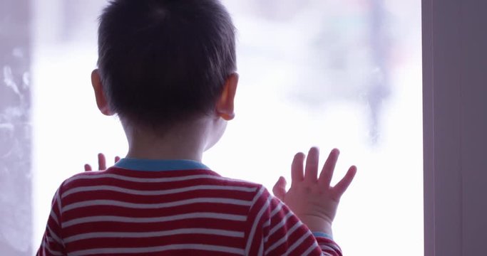 Toddler boy looks out window into white background - from behind