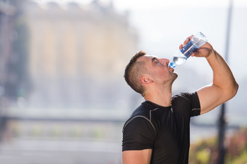 man drinking water from a bottle after jogging