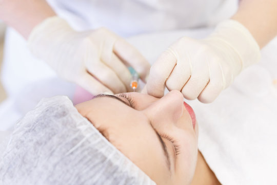 Top view. Close up female face and cosmetologist's hands with syringe during facial beauty injections. Botox pricks, hyaluronic acid injection. Rejuvenation and hydratation. Cosmetology.