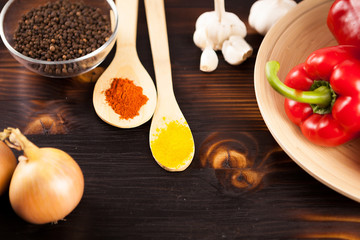Top view on powder spices next to onion, sweet pepper and garlic on burned wooden background