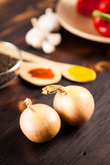 Top close up view on onions with different vegetables blurred on background over burned wooden table
