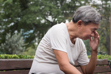 sad hopeless frustrated old retired senior man sitting in public park, urban poverty concept