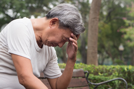 sad hopeless frustrated old retired senior man sitting in public park, urban poverty concept