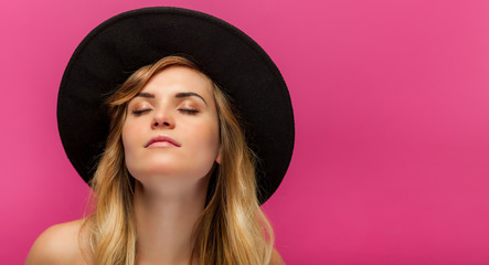 Beautiful young woman with hat and long blonde hair on pink background