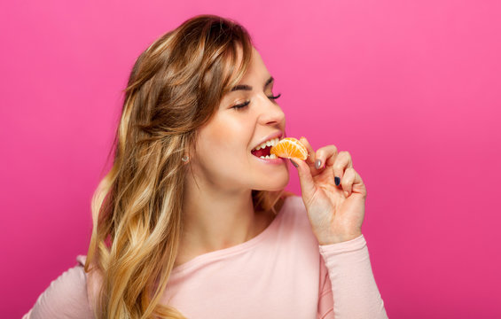 Beautiful Woman On Pink Background Eating Orange Fruit