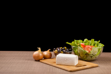 Fresh antipasto from feta cheese, onions and two glass bowls with fresh salad and olives on black background
