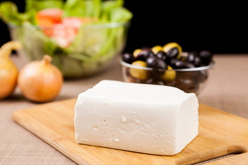 Close up of feta cheese on wooden board on a table ready for serving over black background