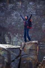 Happy traveler, with open arms, stands on granite stones