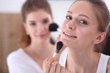 Beautiful girls looking in the mirror and applying cosmetic with a big brush