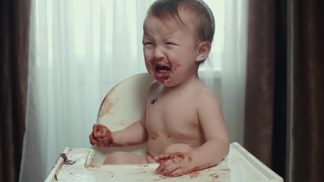 not a happy Asian kid cries, the baby stained his face and hands in chocolate