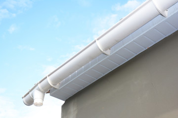 Roof gutter repair. Rain gutter installation with drain downspout pipe. Guttering with soffits and fascia board.