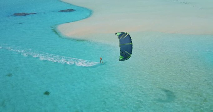Cinematic aerial view of kiteboarder gliding across tropical ocean