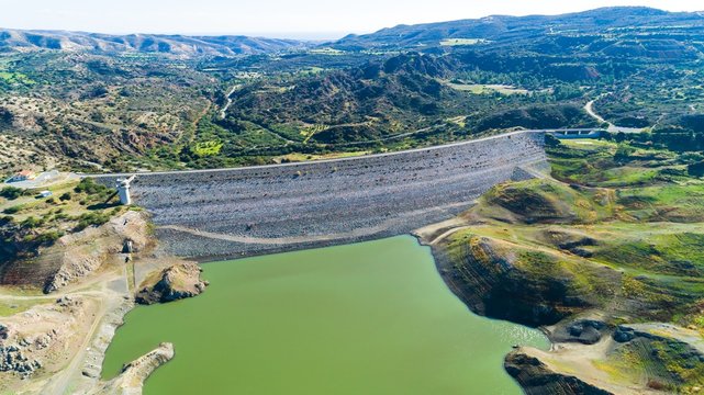 Aerial bird eye view of Kalavasos rockfill dam wall, Larnaca, Cyprus. The street bridge over the reservoir crossing Vasilikos river and the hills around the water from above.