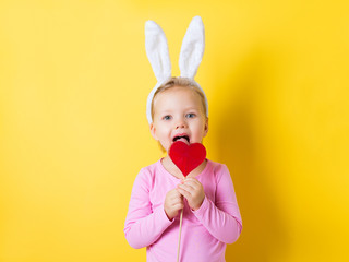 Pretty little girl easter bunny with lollipop or candy on yellow background
