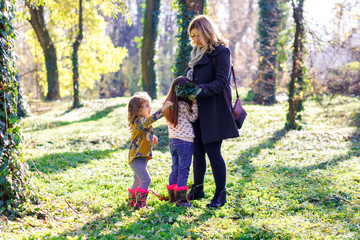 Naklejka na ściany i meble Pregnant mother enjoying with her two daughters in park on sunny autumn day.