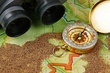 binoculars and a compass on the map with sand