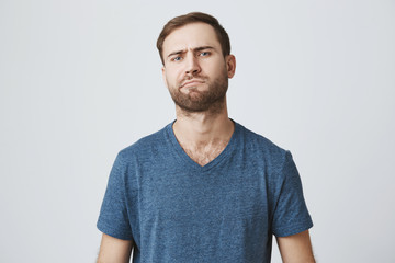 European hesitant bearded man frowns face, thinks over future plans, being little puzzled, poses against gray background. Caucasian male confused and dissatisfied with unexpected news