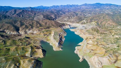 Aerial bird eye view of Kalavasos rockfill dam, Larnaca, Cyprus. The Vasilikos river streaming towards the reservoir, the mountainous landscape and the hills around the water from above.