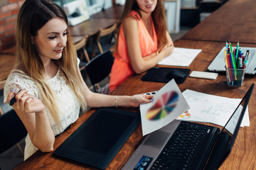 Pretty young female graphic designer looking at color chart sitting at desk in her office